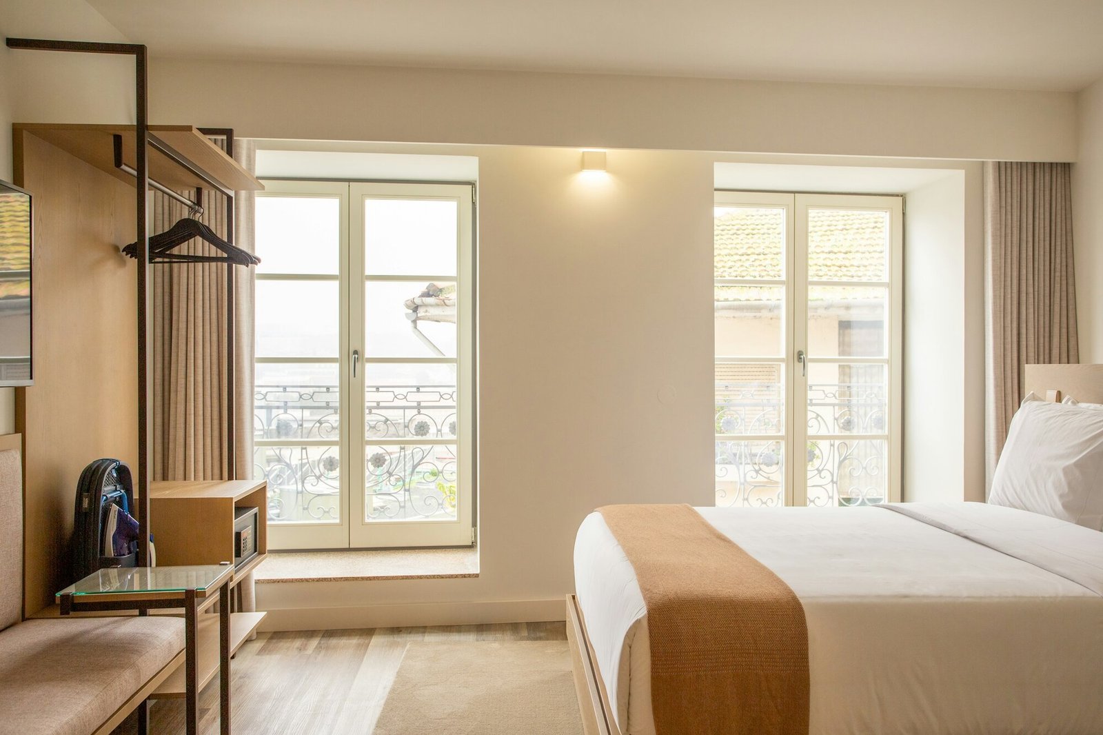 Calm hotel bedroom with French doors opening onto a wrought-iron balcony and warm light.